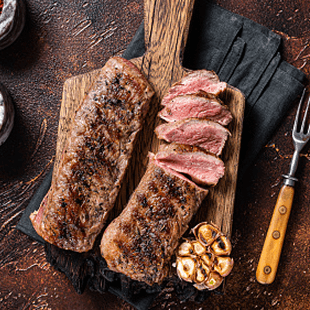 Eine gegrillte Fleischspezialität auf einem Holzbrett mit Knoblauch arrangiert