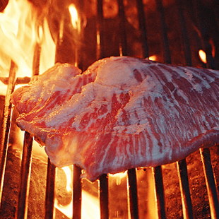 Ein Fleischstück auf einem Grill mit Flammen im Hintergrund